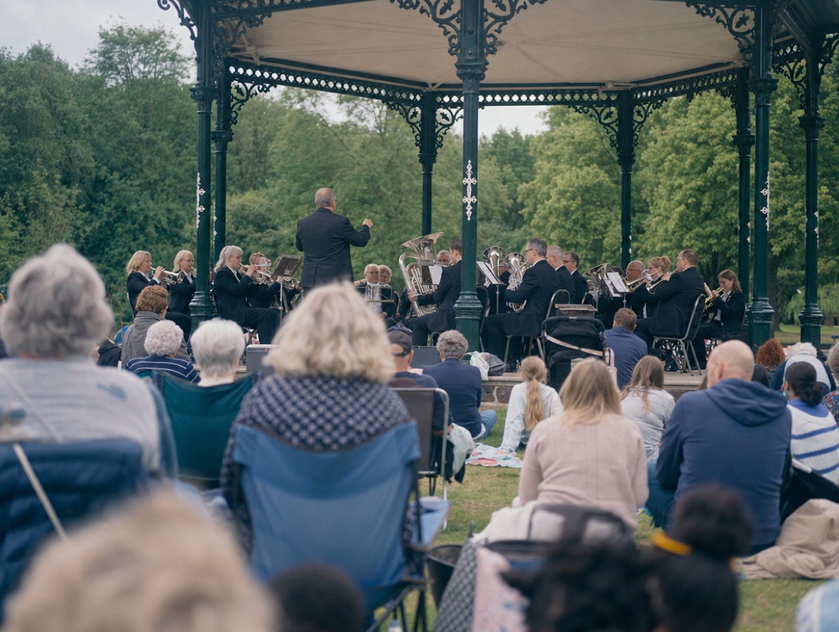 The band playing on a park bandstand on a summer afternoon while families listen from the grass.